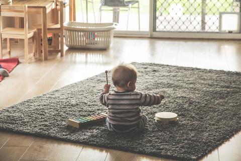 Picture of a baby sitting on a rug, facing away from the camera. Image by thedanw from Pixabay